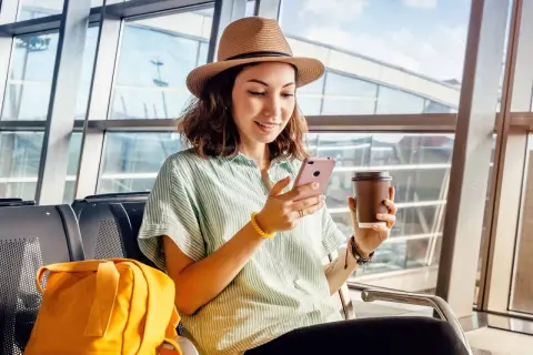 Kobieta w kapeluszu z kawą i telefonem w ręku, gotowa na podróż. Czy to roaming krajowy, czy międzynarodowy, ważne, by mieć łączność.