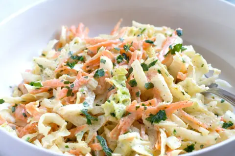 Chinakohl-Salat mit Karottenstreifen und Petersilie in einer weißen Schüssel.