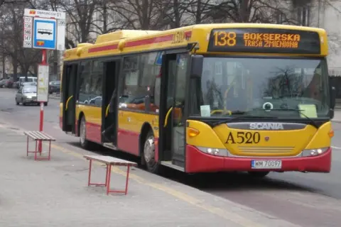 Żółto-czerwony autobus 138 warszawa z otwartymi drzwiami na przystanku.