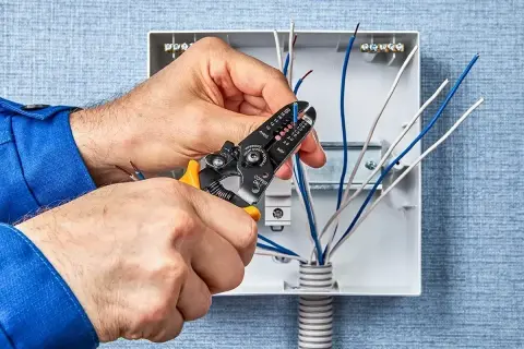 Elektryk zdejmuje izolację z przewodów. Zastanawiasz się, ile zarabia elektryk? To zależy od doświadczenia i regionu.