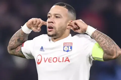 Memphis Depay w koszulce Olympique Lyon, z charakterystycznym gestem. Jego obecne drużyny to FC Barcelona i reprezentacja Holandii.
