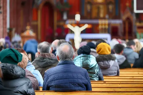 21 kwietnia. Ludzie siedzą w kościele, patrząc w stronę ołtarza z krzyżem.