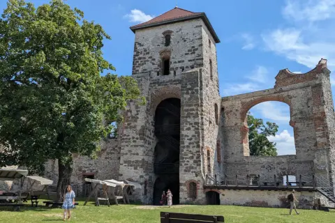 Ruiny zamku Tenczynek z wieżą i łukiem, na tle błękitnego nieba z chmurami.