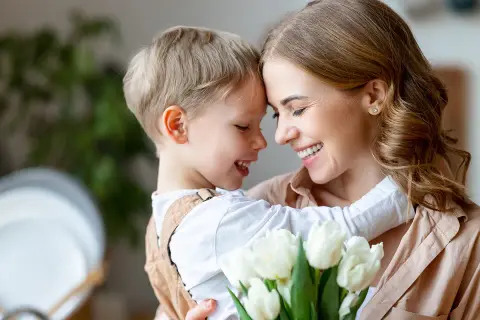 Uśmiechnięta mama i synek przytulają się, trzymając bukiet białych tulipanów. Idealny prezent na 26 maja, Dzień Matki.
