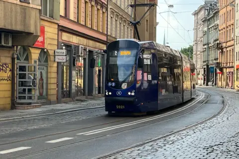 Niebieski tramwaj z napisem "Biskupin" na wyświetlaczu, jadący po brukowanej ulicy w mieście.