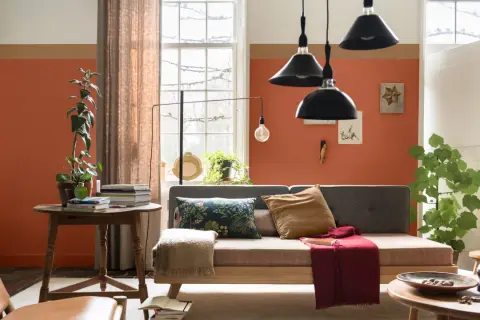 Wohnzimmer mit orangefarbenen Wänden, die mit abriebfester Farbe gestrichen sind. Ein Sofa, ein Tisch mit Büchern und Pflanzen.