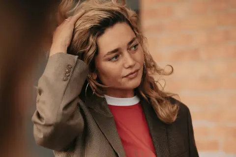 Kobieta z blond włosami w marynarce i czerwonej koszulce, dotykająca włosów.