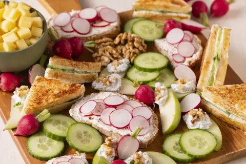 Un plateau d'apéro dinatoire plancha : toasts au fromage frais et radis, mini sandwichs concombre, dés de fromage, noix et quartiers de pomme.