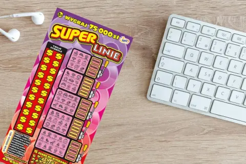 Zdrapka "Super Linie" z symbolami dolara i ikonkami, obok klawiatury i słuchawek.