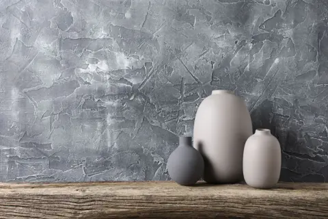 Nowoczesny tynk strukturalny do łazienki w odcieniu szarości, z trzema ceramicznymi wazonami na drewnianej półce.