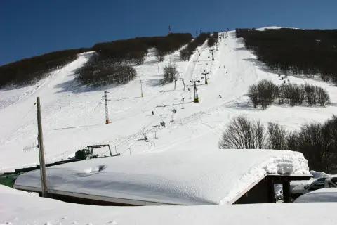 Piste innevate e skilift attivi sul monte Piselli, stazione sciistica con alberi spogli e cielo azzurro.