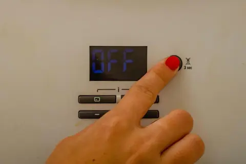 Dito che preme il pulsante per il reset caldaia Immergas. Lo schermo mostra "OFF".