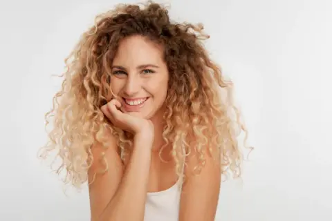Uśmiechnięta kobieta z burzą blond loków, które tworzą piękne **skręty włosów**.