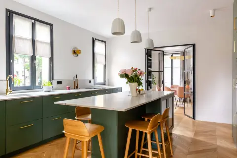 Cuisine moderne avec îlot central, tabourets en bois et armoires vert forêt. Une belle deco cuisine pour un intérieur lumineux.