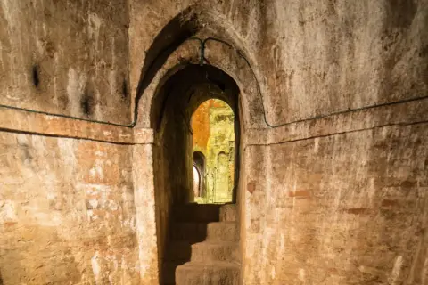Un antico passaggio conduce ai **Bologna canali sotterranei**. Scale di pietra scendono nell'oscurità, tra muri di mattoni e archi in mattoni.