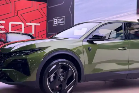 Nowy Peugeot 408 Hybrid w kolorze oliwkowym prezentuje się nowocześnie. Z przodu widoczny jest charakterystyczny grill i reflektory.