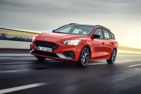 Czerwony Ford Focus sedan ST pędzi po drodze, z rozmytym tłem sugerującym dużą prędkość.