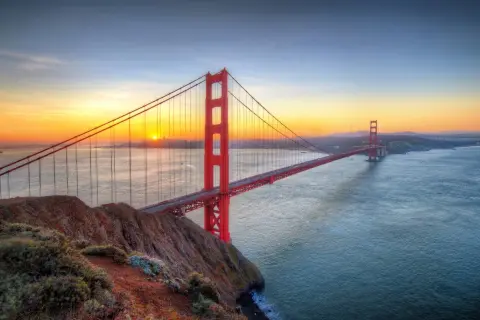 Zachód słońca nad Zatoką San Francisco, gdzie majestatyczny san francisco most rozciąga się nad wodą, a jego czerwone wieże lśnią w złotym świetle.