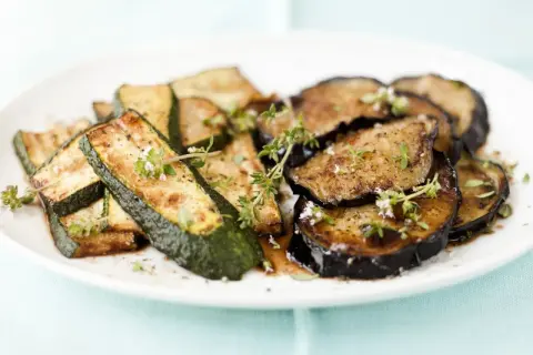 Gebratene zucchini und aubergine in der pfanne, garniert mit frischen Kräutern.
