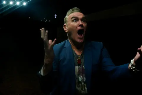 Morrissey en Zaragoza, con gesto dramático y las manos alzadas, bajo luces y una cruz.