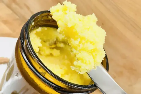 Ein Löffel hebt goldgelbes Ghee Butter aus einem Glas. Was ist Ghee Butter? Ein geklärte Butter, ideal zum Kochen.