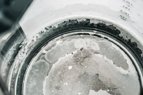 Gros plan sur le fond d'une bouilloire, montrant un tableau de dureté de l'eau avec des dépôts calcaires blancs et grisâtres.