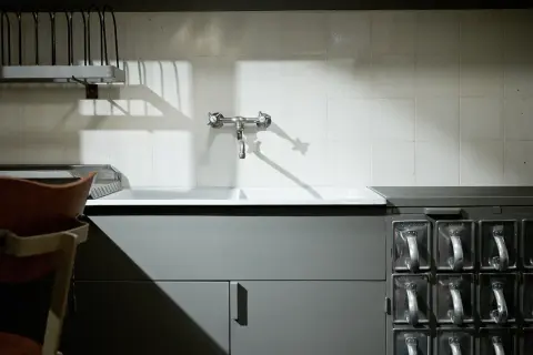 Stara kuchnia frankfurcka z ceramicznym zlewem, kranem i rzędem metalowych pojemników na przyprawy.