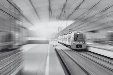 Nowoczesny pociąg pędzi po torach, symbolizując szybki rozwój infrastruktury i wykup gruntów pod kolej.
