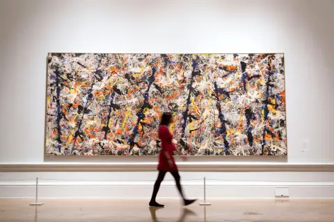 A woman in a red dress walks past a large, vibrant canvas of contemporary abstract expressionism, a masterpiece of splattered paint.