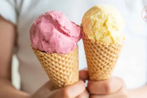 Zwei Eiswaffeln mit frucht eis: eine rosa und eine gelbe Kugel.