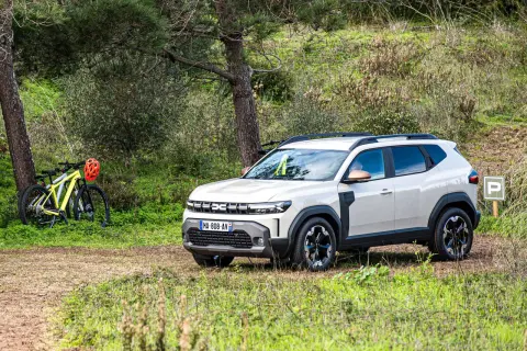 Biały Dacia Duster 1.6 benzyna zaparkowany na leśnej polanie obok rowerów.