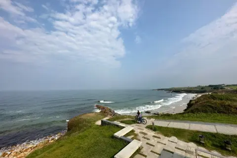 Un paseo en bicicleta por las **playas cerca de Foz**, con el mar Cantábrico de fondo y un cielo nublado.