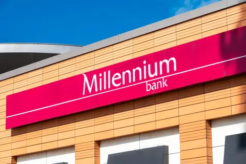 Elegancki budynek z logo Millennium bank. Jasne panele elewacyjne i fuksjowy baner z nazwą banku.