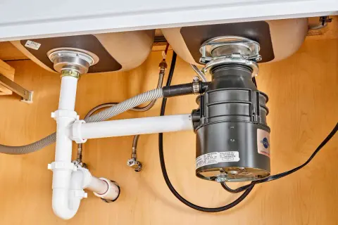 Under-sink plumbing with a garbage disposal installed, showing pipes and connections. This image illustrates how to install a garbage disposal.