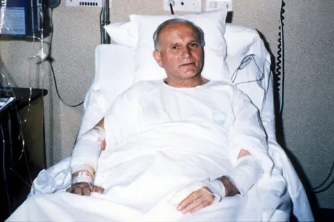 Juan Pablo II en cama de hospital, recuperándose tras el atentado. Sus brazos vendados muestran las secuelas del ataque.