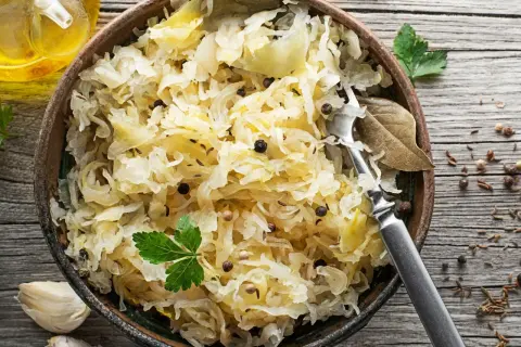 Miseczka pełna aromatycznej surówki z kiszonej kapusty, doprawionej pieprzem i kminkiem. Obok czosnek i buteleczka oleju.