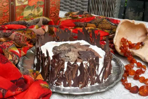 A chocolate-decorated cake with whipped cream and chocolate leaves on top, set on a silver platter.