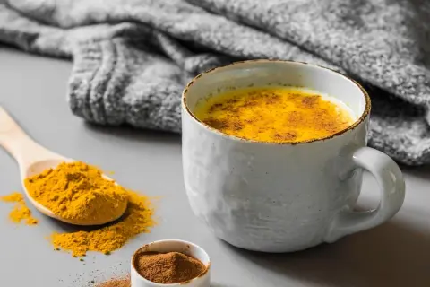 Un latte dorato speziato, perfetto cosa bere al posto del caffè. Curcuma e cannella in una tazza calda, con una coperta grigia sullo sfondo.