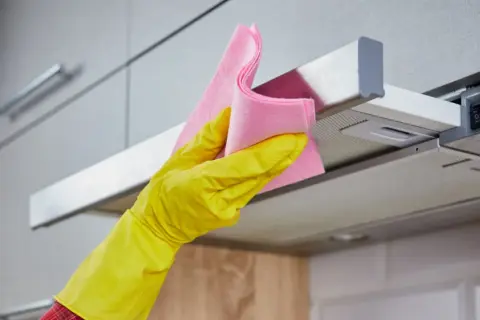 Gelbe Handschuhe und ein rosa Tuch reinigen die klebrige Dunstabzugshaube.