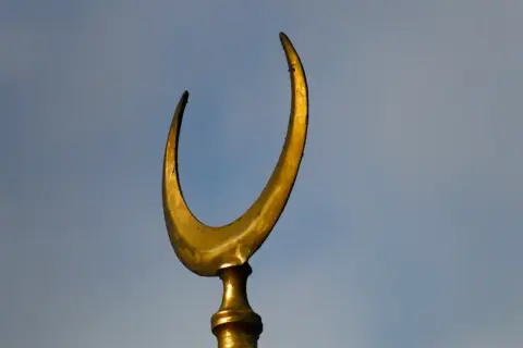 Złoty półksiężyc, symbol meczetu, na tle błękitnego nieba.