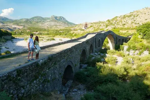Pareja admira un puente de piedra histórico, un lugar perfecto para un viaje a Albania de 5 días.