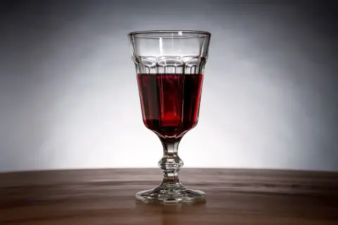 Szklanka z ciemnoczerwonym winem z jeżyn, stojąca na drewnianym blacie.