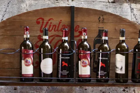 Rząd butelek wina, w tym Chianti Classico, na drewnianym stojaku z napisem "Vintage". Idealne na podróż po regionie Toskania.