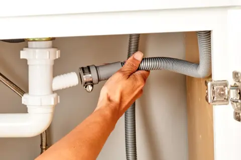 Hand connecting a dishwasher drain hose to a sink drain pipe.
