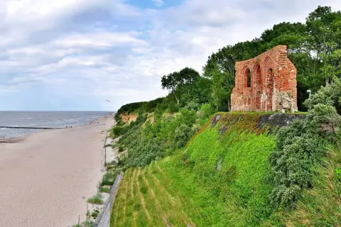 Malownicze klify w Polsce z ruinami ceglanej budowli na szczycie, plaża i morze w tle.