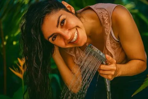Lächelnde Frau spült sich die Haare mit Wasser. Vielleicht ein letzter Spülgang mit Apfelessig für glänzende Haare?