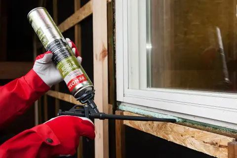 Persona con guantes rojos aplica espuma de poliuretano alrededor de una ventana. Averigua cuanto tarda en secar la espuma de poliuretano para un sellado perfecto.