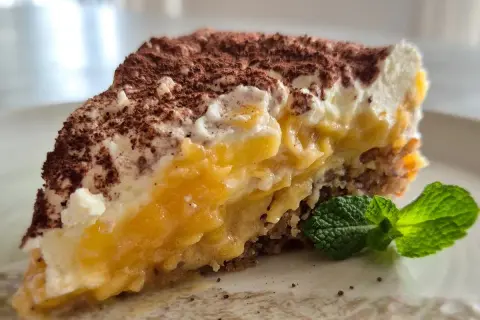 Ein saftiger Apfelkuchen-Schnitte mit cremiger Füllung, Kakao bestäubt und Minze garniert.