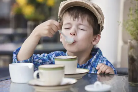 Bambino con cappellino gustando un delizioso cappuccino senza caffè, con gli occhi chiusi per il piacere.