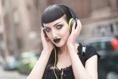 Mroczna goth girl w słuchawkach, z czarną szminką i kolczykiem w nosie, słucha muzyki na ulicy.